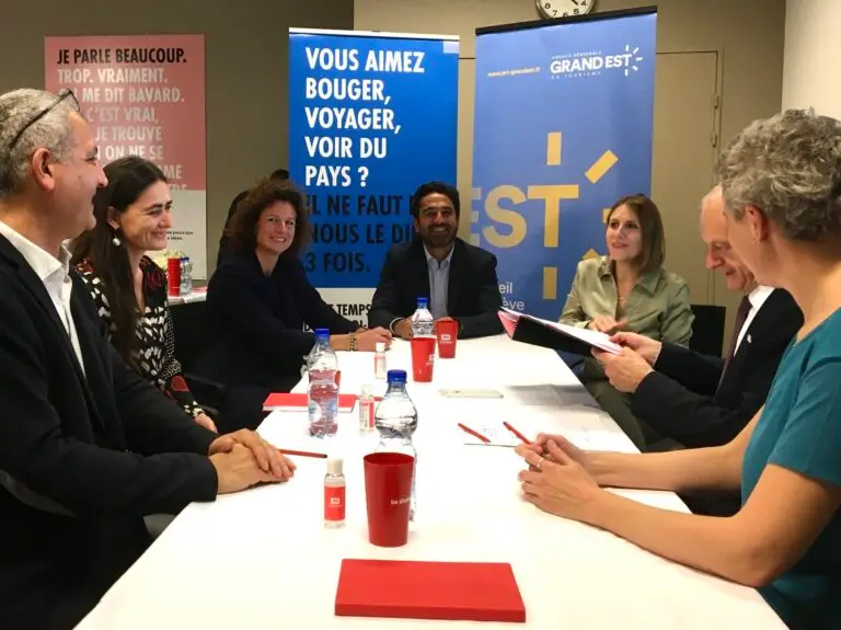 Sept personnes sont assises autour d'une table de réunion, entourées de documents et de bouteilles d'eau, devant des banderoles portant des inscriptions en français, dans une salle de réunion, réunies pour discuter du partenariat exclusif entre l'Agence régionale du tourisme du Grand Est et la Chaire Vin et Tourisme.