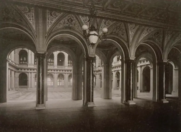 Une arcade somptueuse aux voûtes et colonnes ornées, agrémentée de décors cachés qui murmurent les récits des 80 ans d’histoire du Palais Universitaire, s’ouvrant sur une cour spacieuse entourée d’un bâtiment de plusieurs étages.