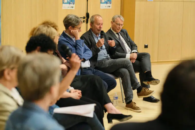 Un groupe de personnes, parmi lesquelles des représentants d’associations d’usagers et de patients, participe à une table ronde dans une salle aux murs en bois clair ; un homme s’exprime au micro tandis que d’autres, parmi lesquels figurent peut-être des mécènes, l’écoutent attentivement.