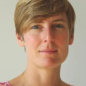 Une personne aux cheveux courts châtain clair et aux yeux bleus regarde l'objectif, vêtue d'un haut rose, sur un fond clair et uni — illustrant ainsi la « différence avant et après » qu'Astrid Chevolet explore dans ses projets au Jardin des Sciences.