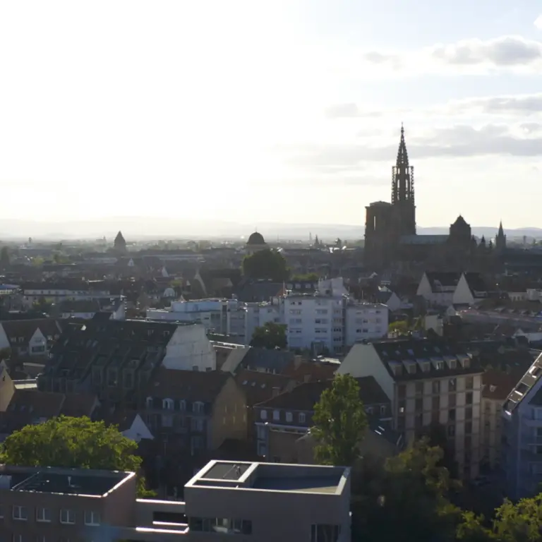 Un paysage urbain mêlant bâtiments modernes et historiques sous un ciel radieux, dominé en arrière-plan par une grande église au clocher élancé, reflète l'esprit de mécénat qui a contribué à façonner son patrimoine architectural et à élargir le goût de donner à travers les générations.