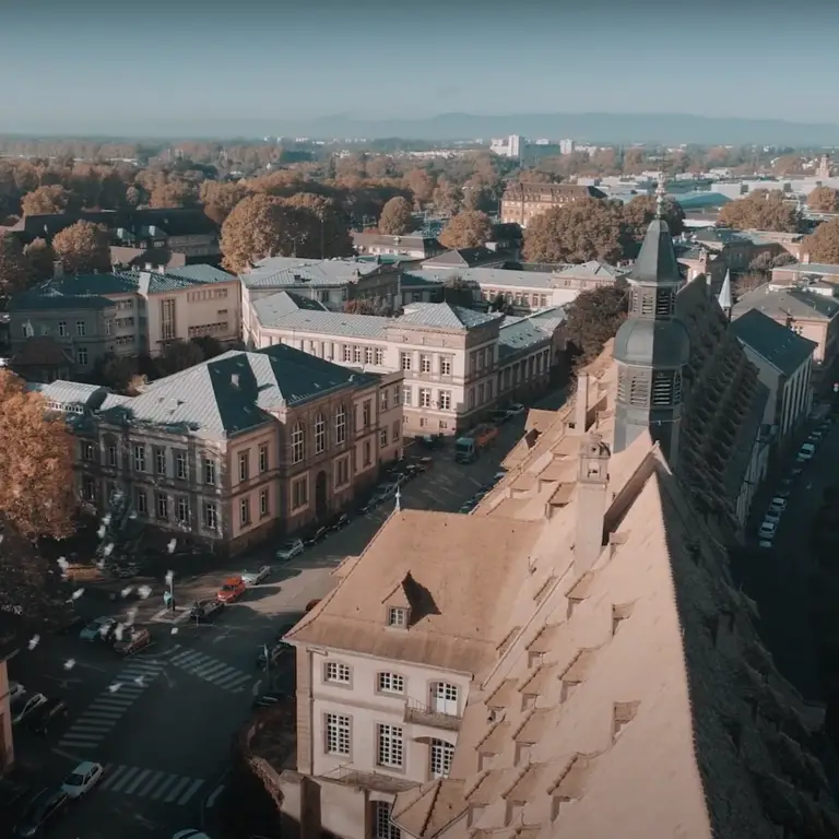 Vue aérienne d'une ville européenne avec ses bâtiments historiques, ses rues bordées d'arbres et ses voitures garées le long des routes par une journée ensoleillée, illustrant l'atmosphère dynamique où les PME (petites et moyennes entreprises) prospèrent aux côtés d'universités de renom.