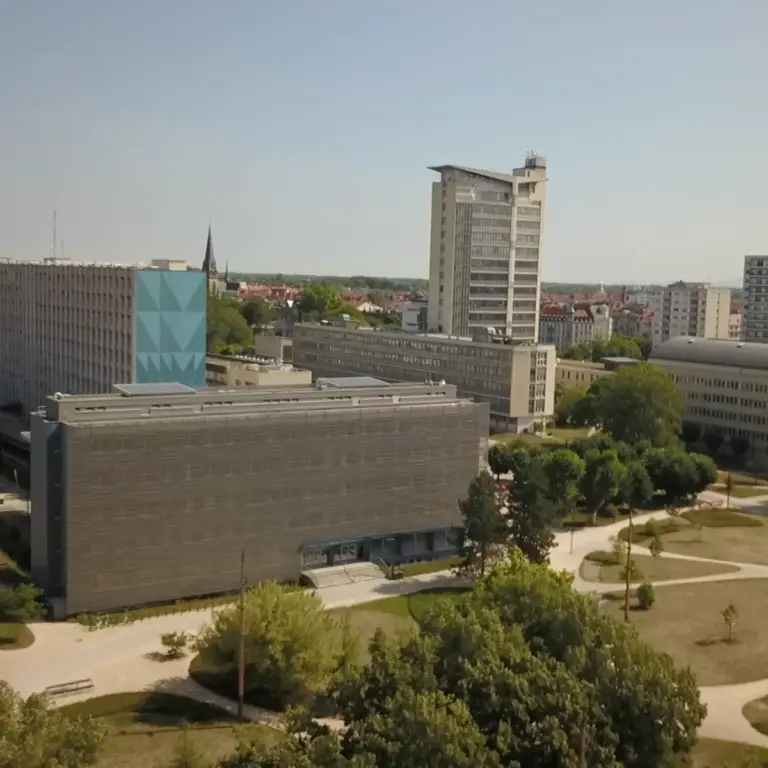Un campus universitaire composé de plusieurs bâtiments modernes, d'allées piétonnes, d'arbres et d'une haute tour sous un ciel dégagé, conçu pour mettre en valeur l'esprit d'innovation et de collaboration au sein de la communauté hospitalo-universitaire.