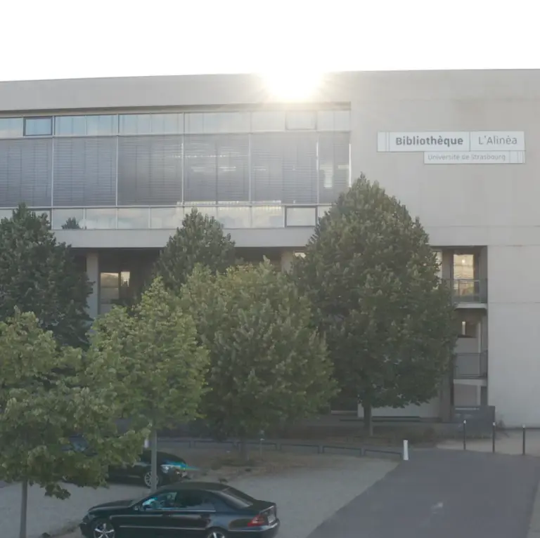 L'extérieur de la Bibliothèque L'Alinéa de l'Université de Strasbourg, avec des arbres et des voitures garées devant, baigné par la lumière du soleil — une illustration de la manière dont le mécénat et les efforts visant à promouvoir l'enseignement supérieur enrichissent à la fois la vie du campus et la communauté locale.
