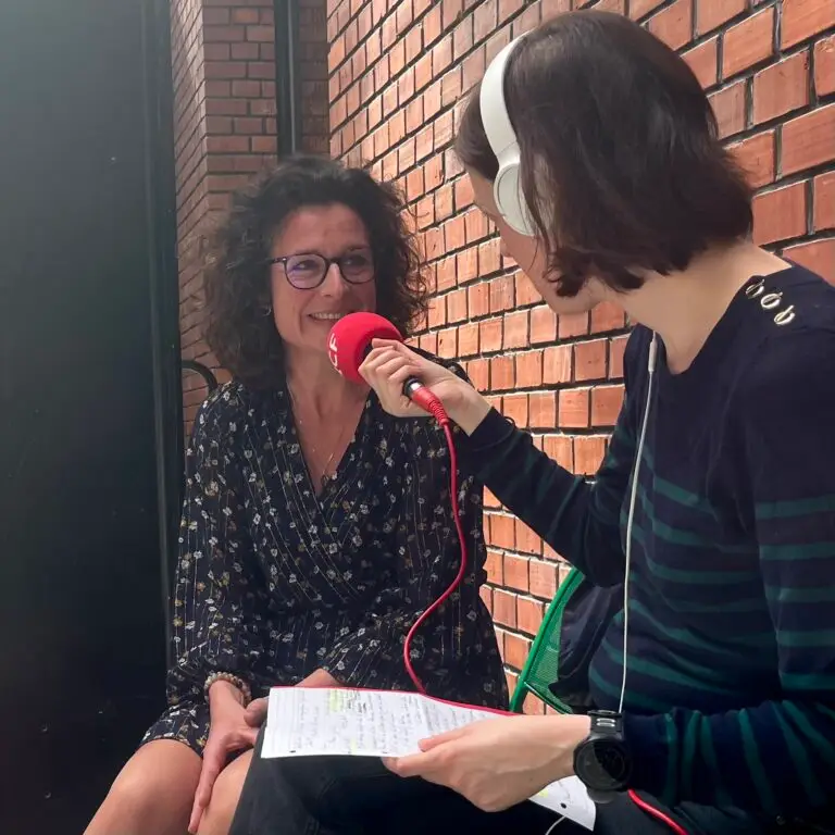 Une personne portant des lunettes est interviewée par une autre personne tenant un micro rouge et un bloc-notes ; toutes deux sont assises près d'un mur de briques. La conversation semble porter sur le travail de Coralie Haller au sein de la Chaire Vin et Tourisme, et met en avant des éléments clés concernant « Talents pour demain ».