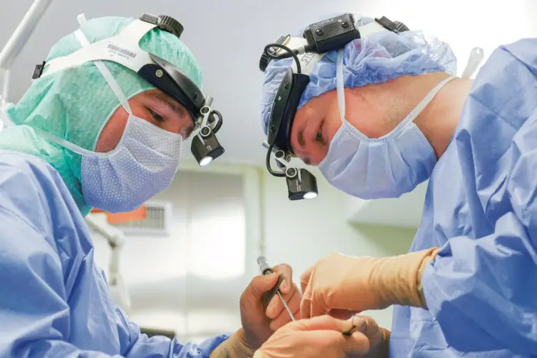Deux chirurgiens, équipés de masques chirurgicaux, de blouses et de lampes frontales, opèrent ensemble dans un bloc opératoire bien éclairé. Ils travaillent avec minutie pour diagnostiquer un cancer du foie, tout en restant concentrés malgré l'écho médiatique que peuvent susciter des cas aussi complexes.