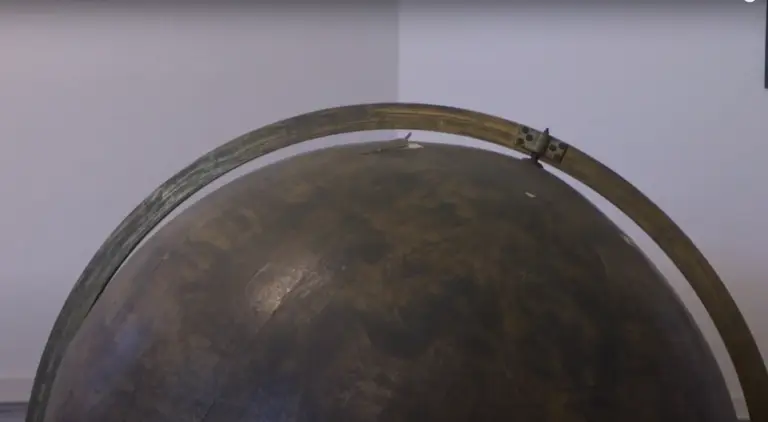 Un gros plan sur la partie supérieure d'un ancien globe de Coronelli de couleur sombre, orné d'un méridien en métal terni, évoque la riche histoire de l'astronomie, sur un fond sobre blanc et gris.