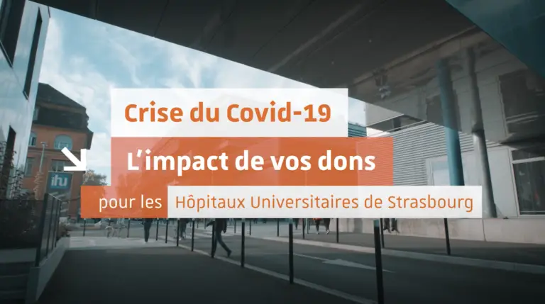 Devant un bâtiment hospitalier moderne, une pancarte sur laquelle on peut lire « Crise du Covid-19 : L’impact de vos dons pour les Hôpitaux universitaires de Strasbourg » met en avant le rôle crucial que les dons ont joué pendant la crise du Covid-19, tandis que des passants défilent à l’extérieur.
