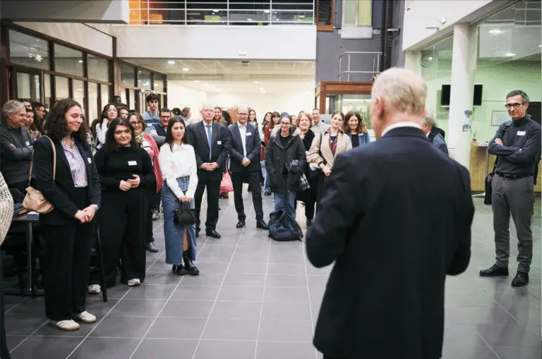 Dans un hall d'accueil spacieux et moderne, un homme en costume s'adresse à l'assistance réunie à l'occasion de la Rencontre annuelle des Bourses des donateurs ; les personnes présentes, debout, écoutent attentivement tandis que les étudiants lauréats sont mis à l'honneur lors de cet événement organisé en salle.