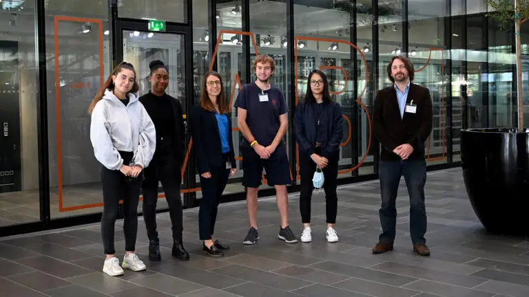 Six personnes se tiennent à l'intérieur, sur un sol carrelé, et posent pour une photo de groupe devant des portes vitrées ornées d'une inscription orange, soulignant leur collaboration à un récent « Compte-rendu d'activité » dans le domaine de la science des données.