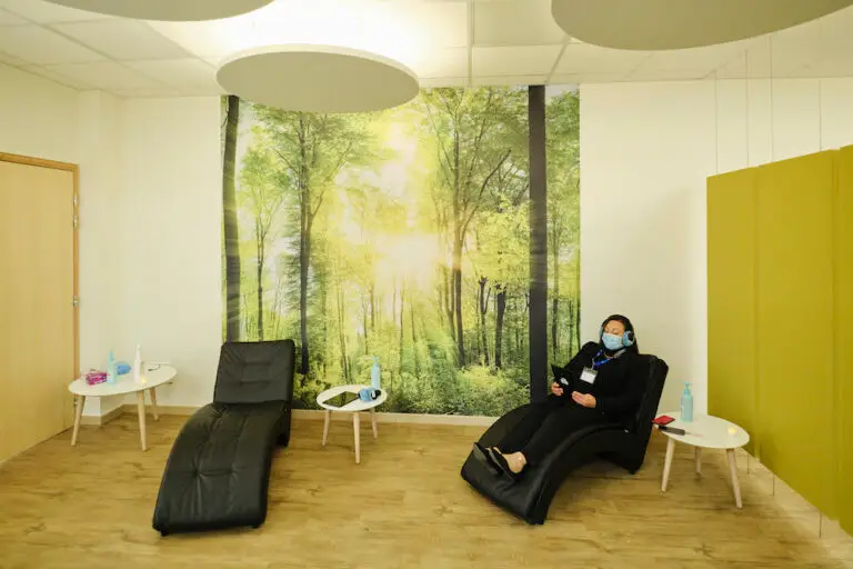 Une personne portant un masque est assise dans un fauteuil inclinable noir, dans un « espace de ressourcement » de l'hôpital de Hautepierre, entourée de décorations murales représentant la forêt, de parquet et de tables d'appoint blanches.