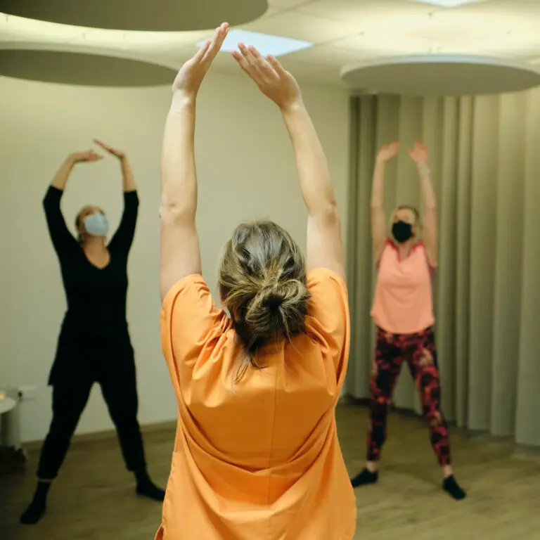 Trois personnes portant des masques se tiennent à l'intérieur, les bras levés, et participent à une séance d'exercices en groupe ou d'étirements dans un espace de ressourcement de l'hôpital de Hautepierre.