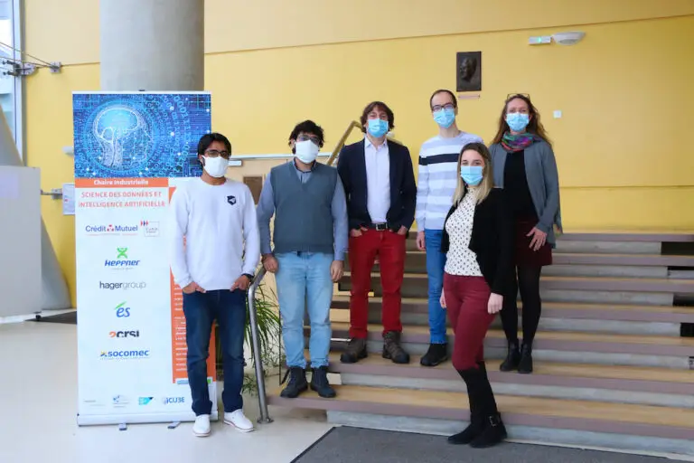 Six personnes portant des masques se tiennent côte à côte dans un couloir près d'un escalier, illustrant les mesures de sécurité liées au Covid ; une bannière promotionnelle arborant des logos est visible sur le côté gauche de l'image, faisant peut-être référence aux avancées en science des données ou en intelligence artificielle.