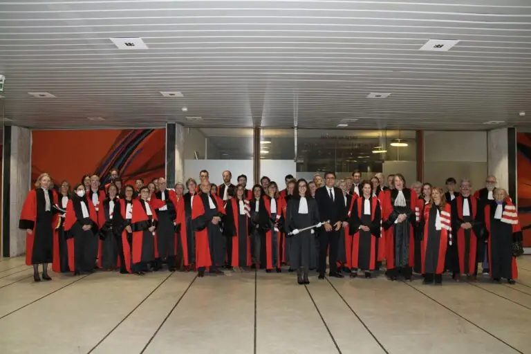 Un grand groupe de personnes vêtues de robes noires rehaussées de touches de rouge se tient rassemblé dans un couloir moderne, posant pour une photo de groupe, afin de célébrer leur excellence et leur engagement lors de la remise des prix.