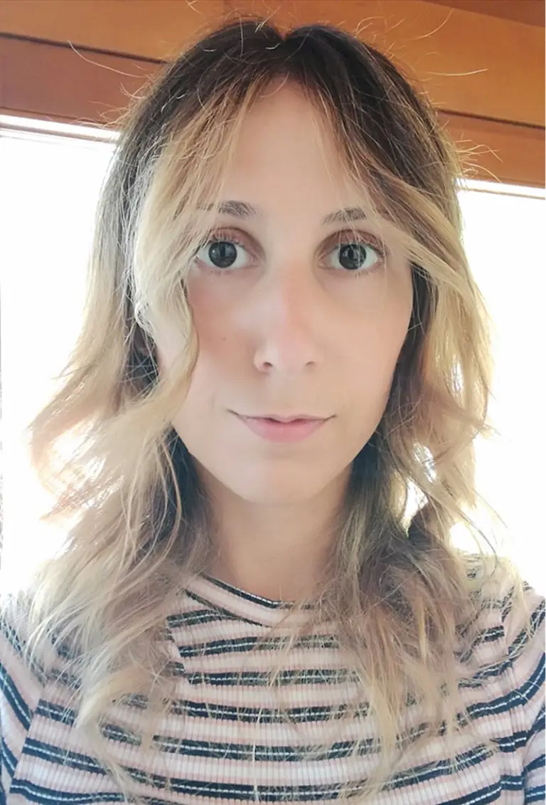 Une personne aux cheveux longs, ondulés et châtain clair, vêtue d'un t-shirt rayé — lauréate du prix ChaMo 2021 — regarde droit vers la caméra avec une expression neutre.