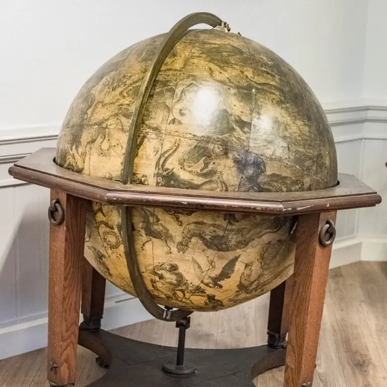 Un globe céleste ancien, orné d'illustrations de constellations sur sa surface, exposé à l'intérieur sur un socle en bois.