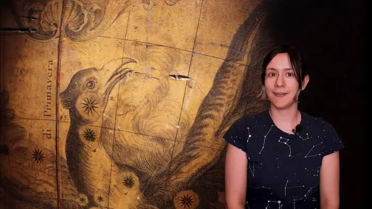 Une femme vêtue d'un t-shirt orné d'un motif représentant des constellations se tient devant une carte du ciel vintage sur laquelle figure l'illustration d'un oiseau et la mention « di Primavera », rappelant le savoir-faire artistique historique que l'on retrouve dans les projets de restauration du globe de Coronelli menés par des experts tels que Manon Liénard, qui se consacrent à la restauration du patrimoine.