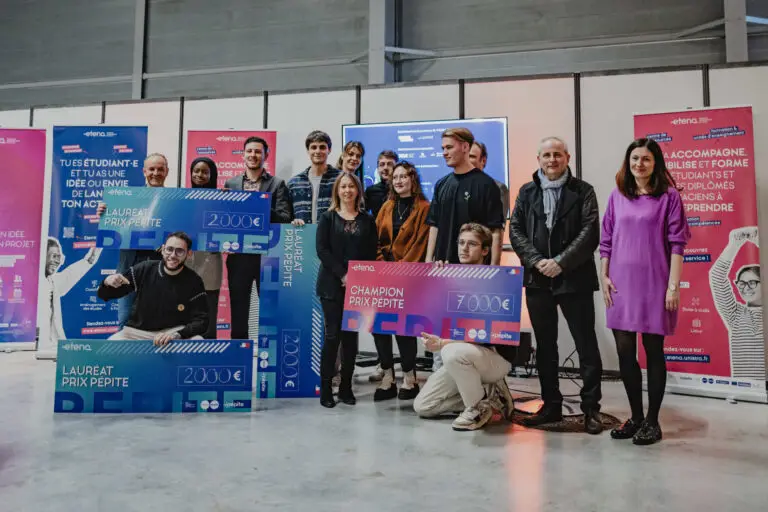 Lors d'une cérémonie de remise des prix, un groupe d'étudiants entrepreneurs pose à l'intérieur, devant des bannières colorées, avec de gros chèques de récompense et des certificats, pour célébrer leurs réussites dans le domaine de l'entrepreneuriat étudiant.