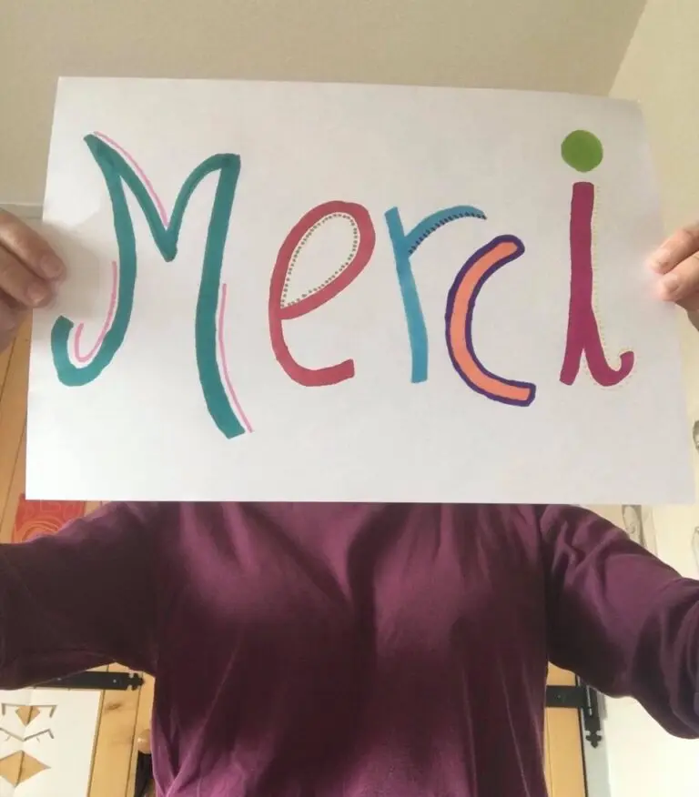 Une personne tenant une pancarte blanche sur laquelle est inscrit le mot « Merci » en grosses lettres colorées, exprimant sa gratitude pour les dons généreux qui ont aidé les étudiants pendant la pandémie de Covid-19.