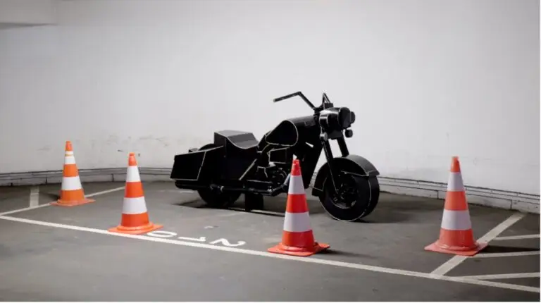 Une moto noire est garée sur une place de stationnement délimitée, entourée de quatre cônes de signalisation orange et blancs, dans un parking couvert aux murs blancs — créant ainsi une scène qui s'apparente presque à de l'art urbain au sein même de cet espace de stationnement bien organisé.