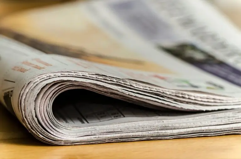 Un journal plié repose sur une surface en bois ; on en aperçoit les bords des pages et une partie du texte imprimé, où des titres évoquant la mobilisation des soignants pendant la pandémie de Covid-19 et le soutien aux étudiants attirent l'attention du lecteur.