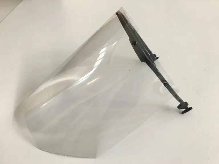 Une visière en plastique transparent, dotée d'un bandeau noir réglable, repose sur une surface blanche. Elle a été fabriquée dans le cadre du « projet solidaire » lancé par l'INSA de Strasbourg pour fournir des visières anti-Covid.