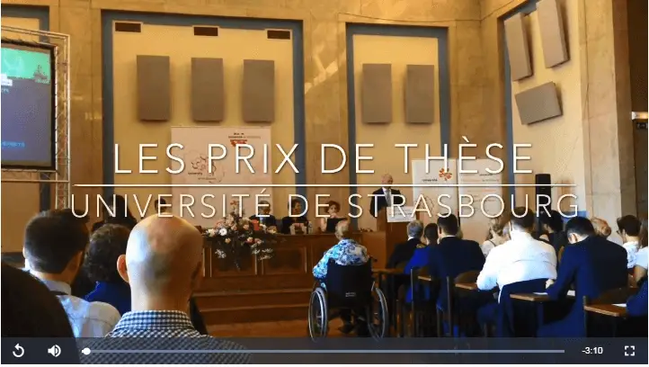 Des personnes assises dans un amphithéâtre assistent à une présentation sur scène lors de la cérémonie des Prix de thèse de l'Université de Strasbourg.